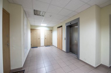 Döşeme döşemesi, ahşap kapıları ve şık bir asansörü olan parlak ve temiz bir apartman koridoru. Konut ilanları, emlak reklamları veya iç tasarım vitrinleri için ideal