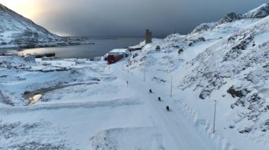 Karlı yamaç kıyısı Honningsvag şehri manzarası virajlı bir yol, uzakta su var. Motorsikletler karla kaplı yolda gidiyor. Norveç