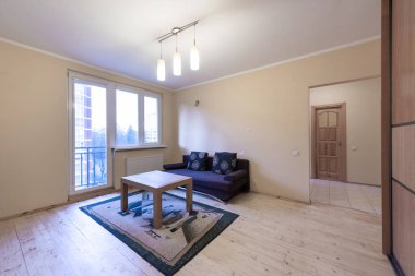 Ev Salonu ve Yatak Odası. Şık bir daire. Açık Alan, kanepe, kanepe ve dolap. Ahşap döşeme ve halı. Kahve masası. LED Işık Pencereleri ve Balkon Kapısı. Geniş Açı