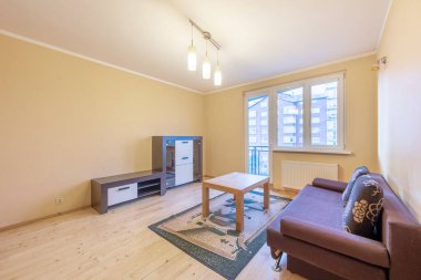 Ev Salonu ve Yatak Odası. Şık bir daire. Açık Alan, kanepe, kanepe ve dolap. Ahşap döşeme ve halı. Kahve masası. LED Işık Pencereleri ve Balkon Kapısı. Geniş Açı