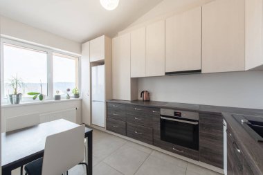 Modern beyaz dolapların, sıcak ahşap tezgahların ve yemek alanının yer aldığı parlak ve minimalist mutfak.