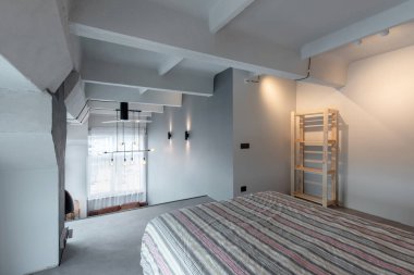 Geniş, modern tavan arası yatak odası, minimalist dekorlar, geniş pencerelerden yansıyan doğal ışık ve şık, açık planlı estetik. Sakin ve nötr ortam gevşemeyi teşvik ediyor.