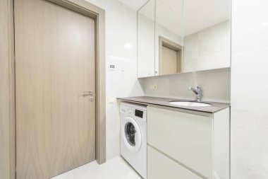 Ev içi çamaşır makinesi, parlak lavabo tasarımı, ahşap kapı ve ev içi rahatlığı ve işlevselliği için mükemmel modern tarzı geliştiren duvar aynaları olan çağdaş bir banyo..