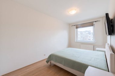 Konforlu ve modern ev minimalist yatak odası. İçinde yeşil bir yatak örtüsü, ahşap döşeme ve camdan süzülen doğal ışık var.