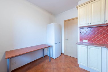 Açık ahşap dolaplar, kırmızı fayanslar, buzdolabı ve yemek masası içeren parlak ve temiz bir mutfak.