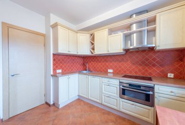 Parlak ve temiz mutfak, hafif ahşap dolaplar, kırmızı fayanslı kaplama, paslanmaz çelik eşyalar, ve parlak bir soba tasarımı.