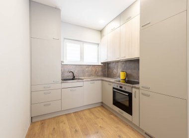 Bej kabin, ahşap zemin ve minimalist bir tasarım içeren çağdaş mutfak düzeneği, küçük alanlar için işlevsellik ve tarz sunar.