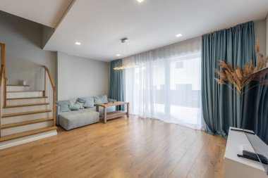 Bir merdiven, rahat bir kanepe ve doğal ışıklandırma ve katıksız perdelerle tamamlanmış ahşap bir masa içeren parlak ve şık bir yaşam alanı.