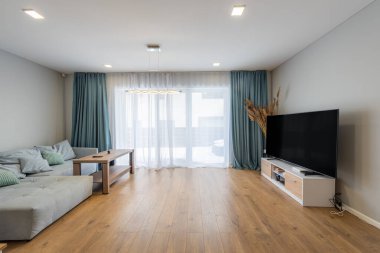 Bir merdiven, rahat bir kanepe ve doğal ışıklandırma ve katıksız perdelerle tamamlanmış ahşap bir masa içeren parlak ve şık bir yaşam alanı.