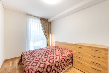 Parlak ve davetkar yatak odası tasarımı ahşap mobilyalar, sıcak tonlamalar, desenli yatak örtüsü ve perdelerin arasından geçen güneş ışığı.