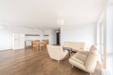 Parlak modern oturma odasında bej mobilyalar, açık mutfak alanı ve ahşap döşemeler var. Minimalist iç tasarım ve modern ev estetiği için ideal.