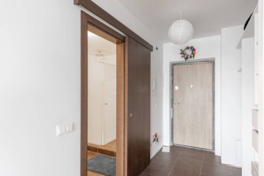 Çağdaş bir iç mekan, ahşap sürgülü kapı, aksesuarlar ve temiz bir atmosfer içeren parlak ve davetkar bir giriş salonu tasarımı.