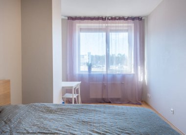 Parlak ve ferah modern yatak odası rahat bir yatak odası, minimalist mobilyalar ve davetkar bir dekor. Doğal ışık, akan perdelerle büyük pencereden akar.