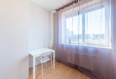 Parlak ve havadar minimalist bir oda, beyaz bir masa, sandalye ve güneş ışığı sakin bir atmosfer için perdelerin arasından akıyor.