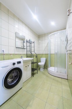 Geniş, modern banyo köşeli bir duş ünitesi, çamaşır makinesi, lavabo ve yumuşak ışıklandırmanın altında yeşil aksanlı duvarları olan tuvalet.