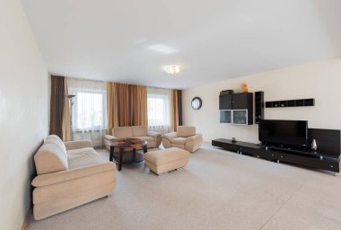 Bej döşemeli mobilyalar, modern eğlence ünitesi ve geniş pencereli geniş doğal ışık sağlayan oturma odası.