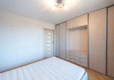 Temiz bir tasarımı, rahat bir yatağı ve pratik mobilyaları olan parlak ve minimalist bir yatak odası.