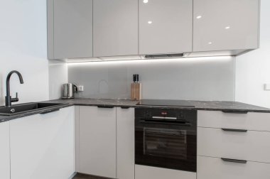 Zarif ve işlevsel bir iç mekan için beyaz minimalist dolap, siyah bir tezgah ve entegre ışıklandırma içeren gösterişli modern mutfak tasarımı