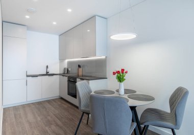 Beyaz dolapları, ahşap döşemeleri, zarif sandalyeler ve canlı bir vazo çiçekle vurgulanmış rahat bir yemek alanı olan parlak, şık bir mutfak tasarımı.