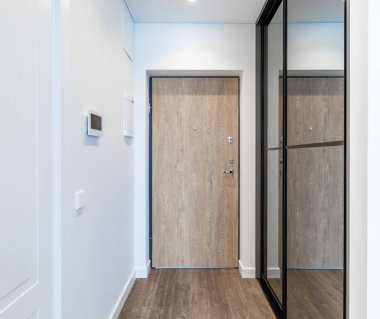 Temiz ve minimalist bir ev girişi ahşap bir kapı, yan ayna ve şık bir tasarım sergiliyor..