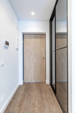 Temiz ve minimalist bir ev girişi ahşap bir kapı, yan ayna ve şık bir tasarım sergiliyor..