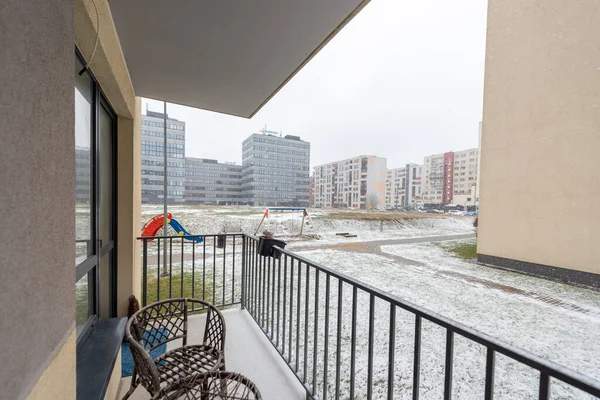 Karlı bir kış gününde modern apartman binalarına bakan rahat bir balkon, dinlenmek için ayarlanmış sandalyeler ve sakin bir açık hava ortamı.