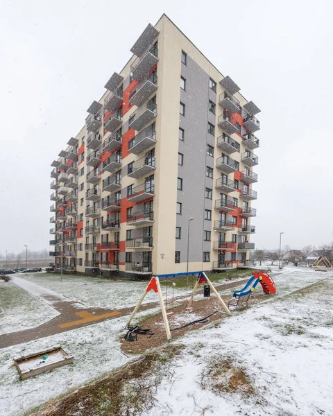 Şehir parkında hafif kar yağışı, salıncaklar, kaydırak ve çıplak ağaçlarla çevrili ıssız bir oyun alanı.
