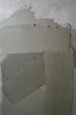 Notched troweling mortar onto a concrete wall in preparation clipart