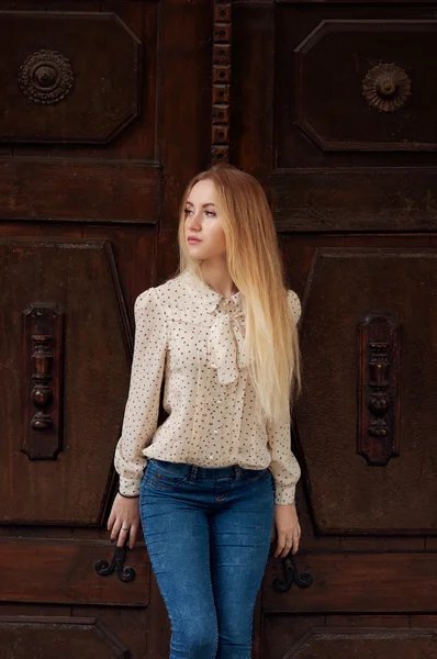 Vacker ung blond flicka i jeans står nära gamla dörr Royaltyfria Stockfoton