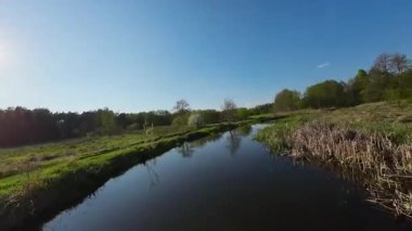 Nehir ve çayır üzerinde alçak ve hızlı bir İHA uçuşu.