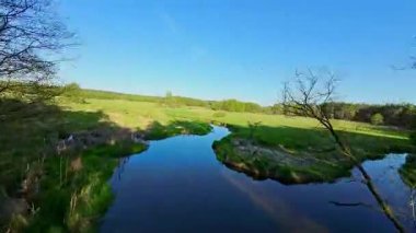 Nehir ve çayır üzerinde alçak ve hızlı bir İHA uçuşu.