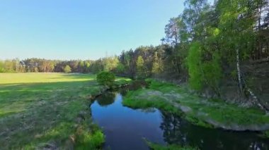Nehir ve çayır üzerinde alçak ve hızlı bir İHA uçuşu.