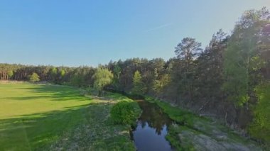 Nehir ve çayır üzerinde alçak ve hızlı bir İHA uçuşu.