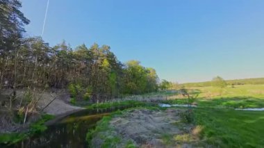 Nehir ve çayır üzerinde alçak ve hızlı bir İHA uçuşu.