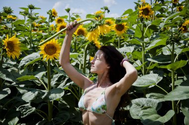 Kafkasyalı genç bir kadının yaz otlağı arka planında duş alırken ayçiçeğiyle poz vermesi..