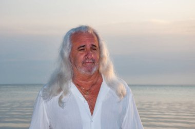 Sanatsal yalnızlık. Su kenarında huzur. Stresten kaçıyorum. Deniz kenarında rahat bir emeklilik hayatı. Gün batımı ışınları. Gün batımında deniz kenarında duran uzun gümüş saçlı yaşlı adam. Yaz denizi kumsalı gün doğumu.