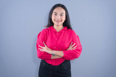 Pembe tişörtlü gülümseyen bir kadın kollarını kavuşturmuş duruyor.