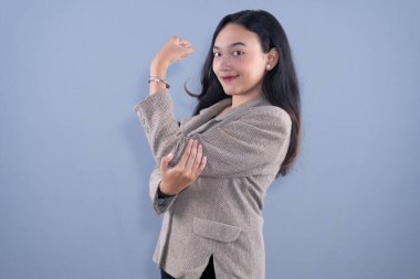 Bej ceketli, gülümseyen bir kadın kaslarını esnetiyor ve gücünü gösteriyor.