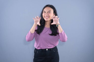 Lavanta gömlekli, gülümseyen bir kadın gri arka plana karşı neşeli bir pençe hareketi yapar.