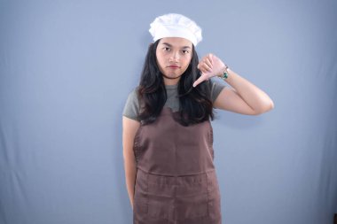 Aşçı şapkalı ve kahverengi önlüklü bir kadın baş parmağını kaldırıyor.