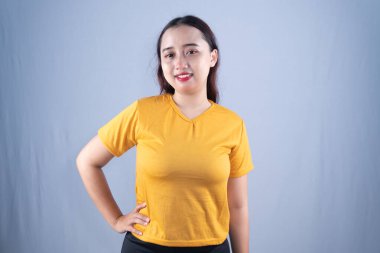 Sarı tişörtlü gülümseyen bir kadın elleri kalçasında durur.