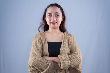 Bej bir hırka giymiş gülümseyen bir kadın kollarını kavuşturmuş duruyor.