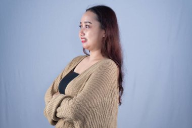 Bej bir hırka giymiş gülümseyen bir kadın kollarını kavuşturmuş duruyor.