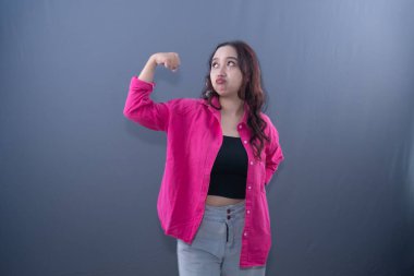 Pembe gömlekli somurtkan bir kadın pazılarını esnetir, gücünü gösterir.