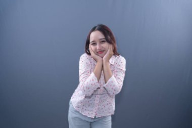 Elleri yanaklarında beyaz çiçekli bir gömlek içinde gülümseyen bir kadın.