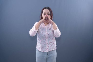 Beyaz gömlekli genç bir kadın elleri ağzında bağırıyor.