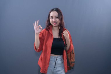 Turuncu gömlekli, gülümseyen bir kadın iyi bir el hareketi yapar.