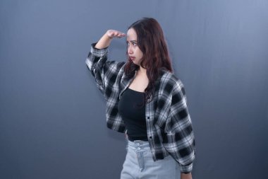 Siyah beyaz ekose gömlekli bir kadın eli alnında ileriye bakıyor.