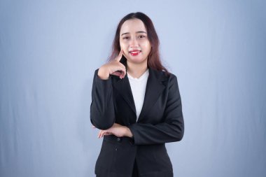 Siyah ceketli bir kadın çenesinde işaret parmağıyla gülümsüyor.