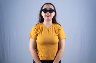 Sarı tişört ve siyah kedi gözü gözlüklü bir kadın kameraya güvenle gülümsüyor.